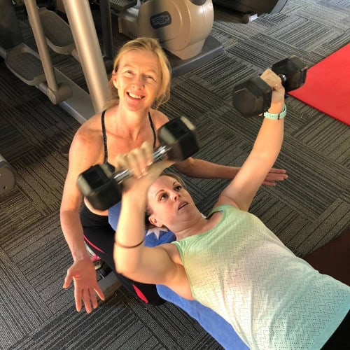 Shedit personal trainer Deb, smiling whilst working with young woman lying on her back and lifting weights